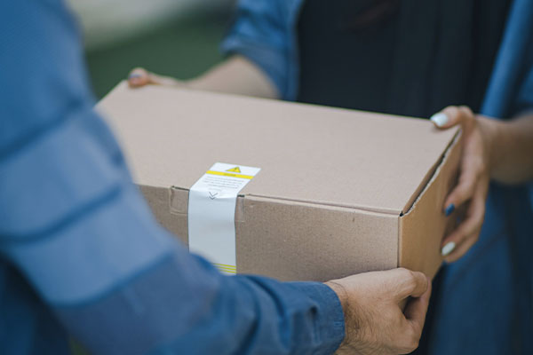 A person handing a shipping box to another person, closeup on hands and box