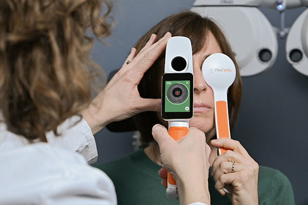 Optometrist refracting a patient in the exam chair with a QuickSee Free Pro, with a phoropter in the background