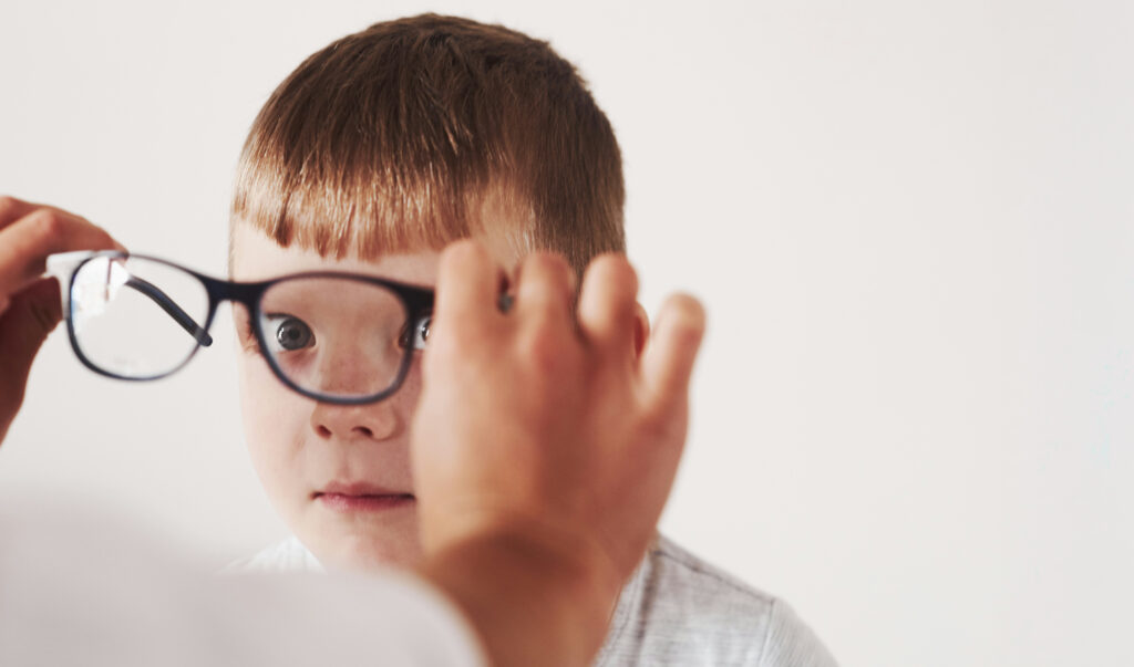 Little boy looking into the camera as he's being fitted with new prescription eyeglasses